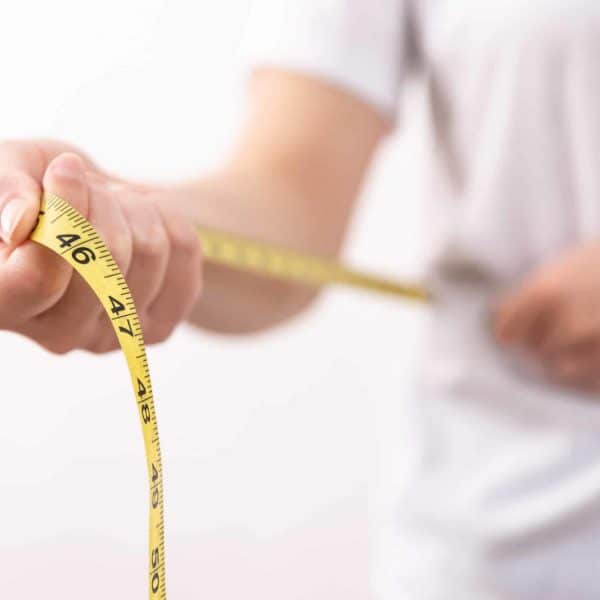 A woman in a white t-shirt holds a yellow centimeter tape in her hands. The concept of losing weight, gaining weight.